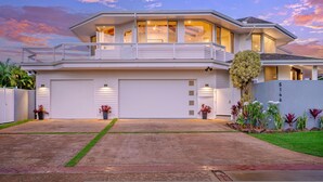A modern two-story house with a large garage, a balcony, and a well-maintained front yard with various plants. - Hanalei Vista Estate (Princeville)