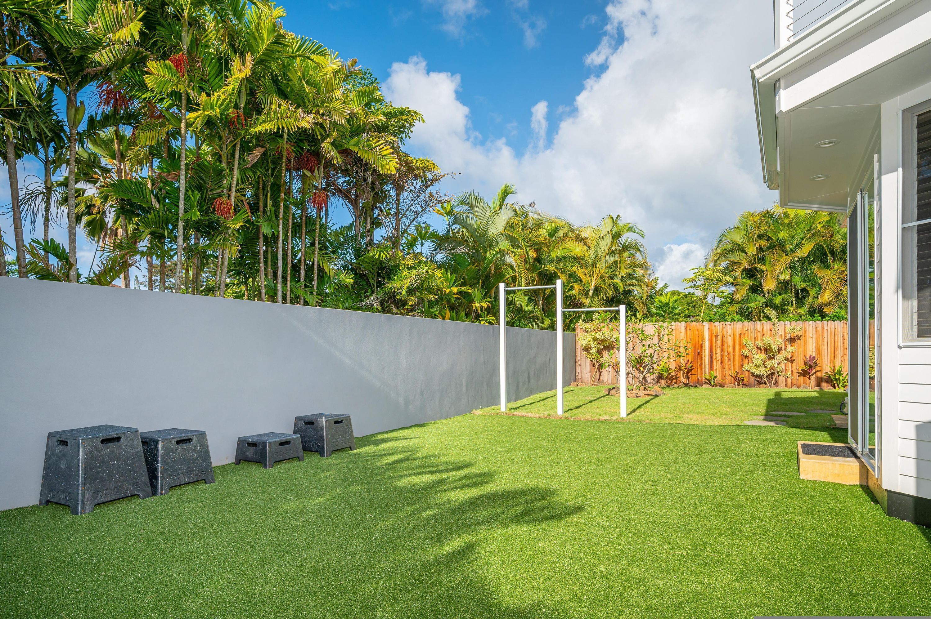 Un patio con césped artificial, una pared blanca y una valla de madera.
