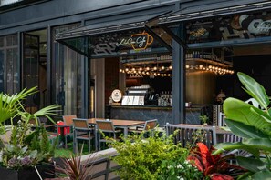 Uma área externa com mesas e cadeiras, um bar com luminárias pendentes e um letreiro neon.