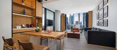 Una cocina moderna con armarios de madera, un comedor con sillas, un sofá negro y vistas a la ciudad a través de amplios ventanales.