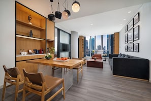 Una cocina moderna con armarios de madera, un comedor con sillas, un sofá negro y vistas a la ciudad a través de amplios ventanales.