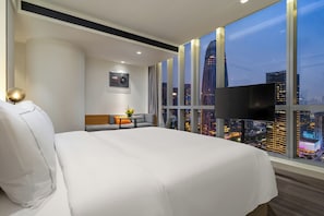 Habitación de hotel con una cama grande, televisión, sofá y vistas a la ciudad.