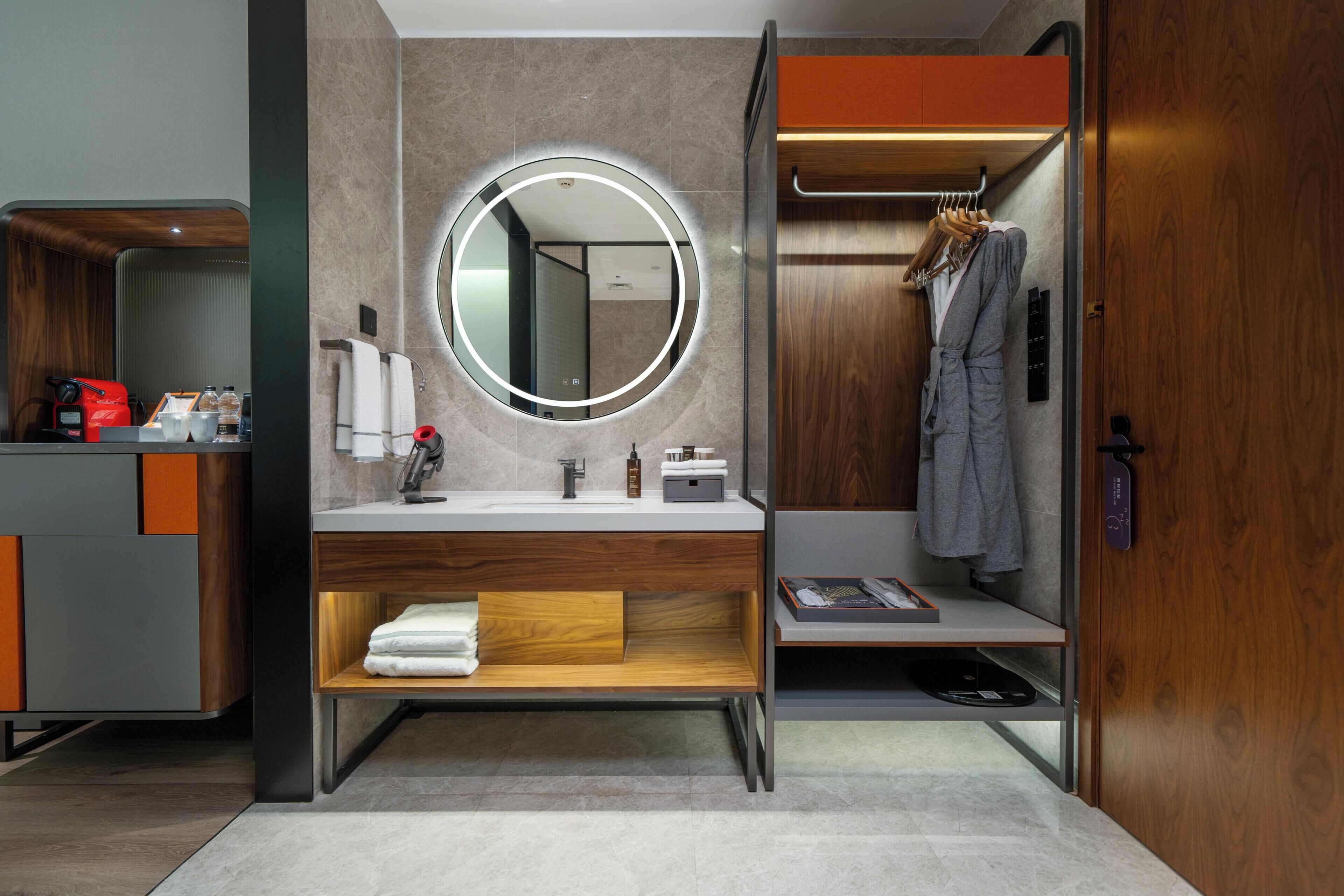 A modern bathroom with a round mirror, wooden vanity, and a robe rack.