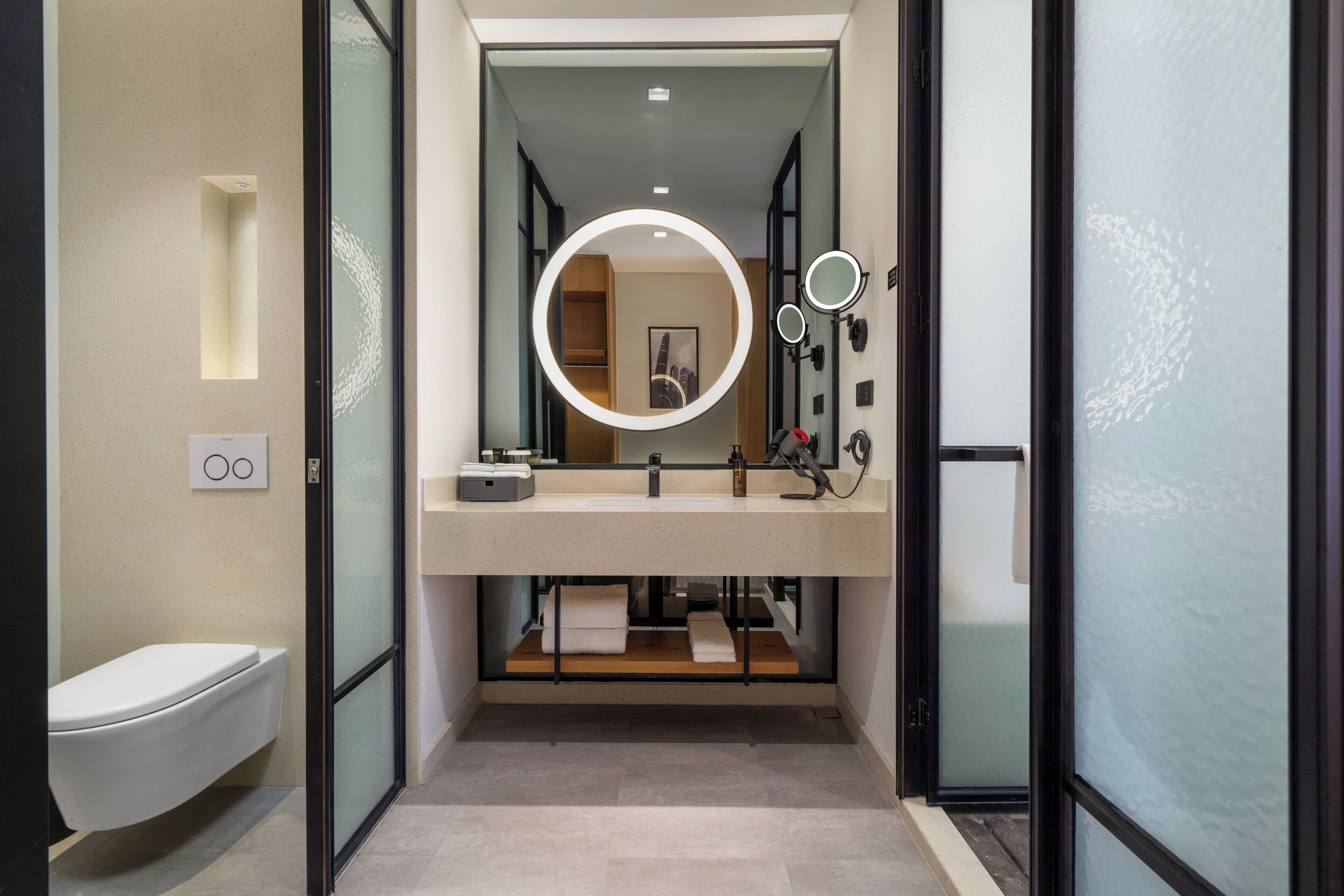 A modern bathroom with a toilet, a vanity with a mirror, and a towel rack.