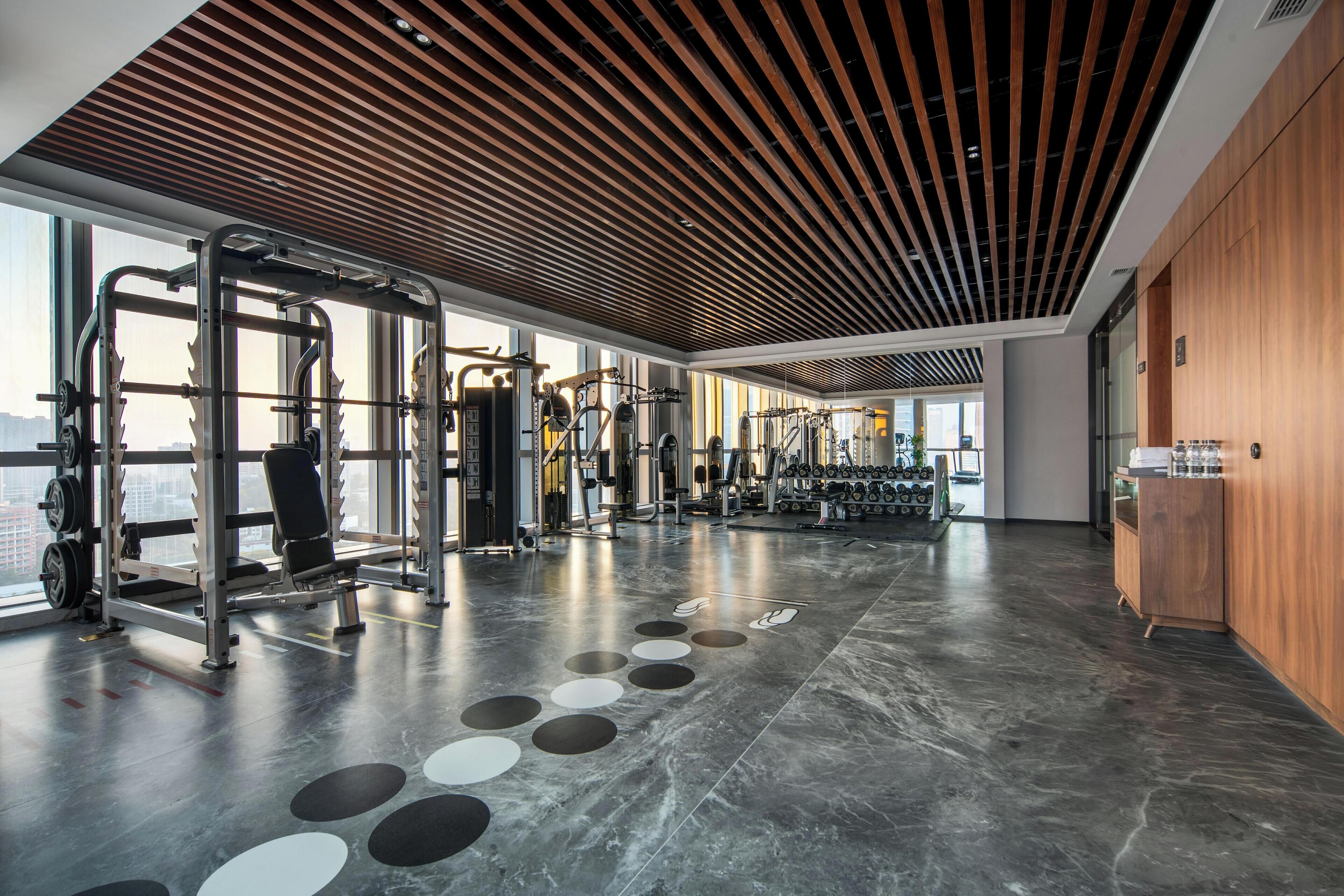 A spacious gym with various exercise equipment, large windows, and a modern ceiling design.