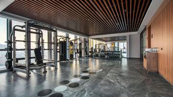 A spacious gym with various exercise equipment, large windows, and a modern ceiling design.