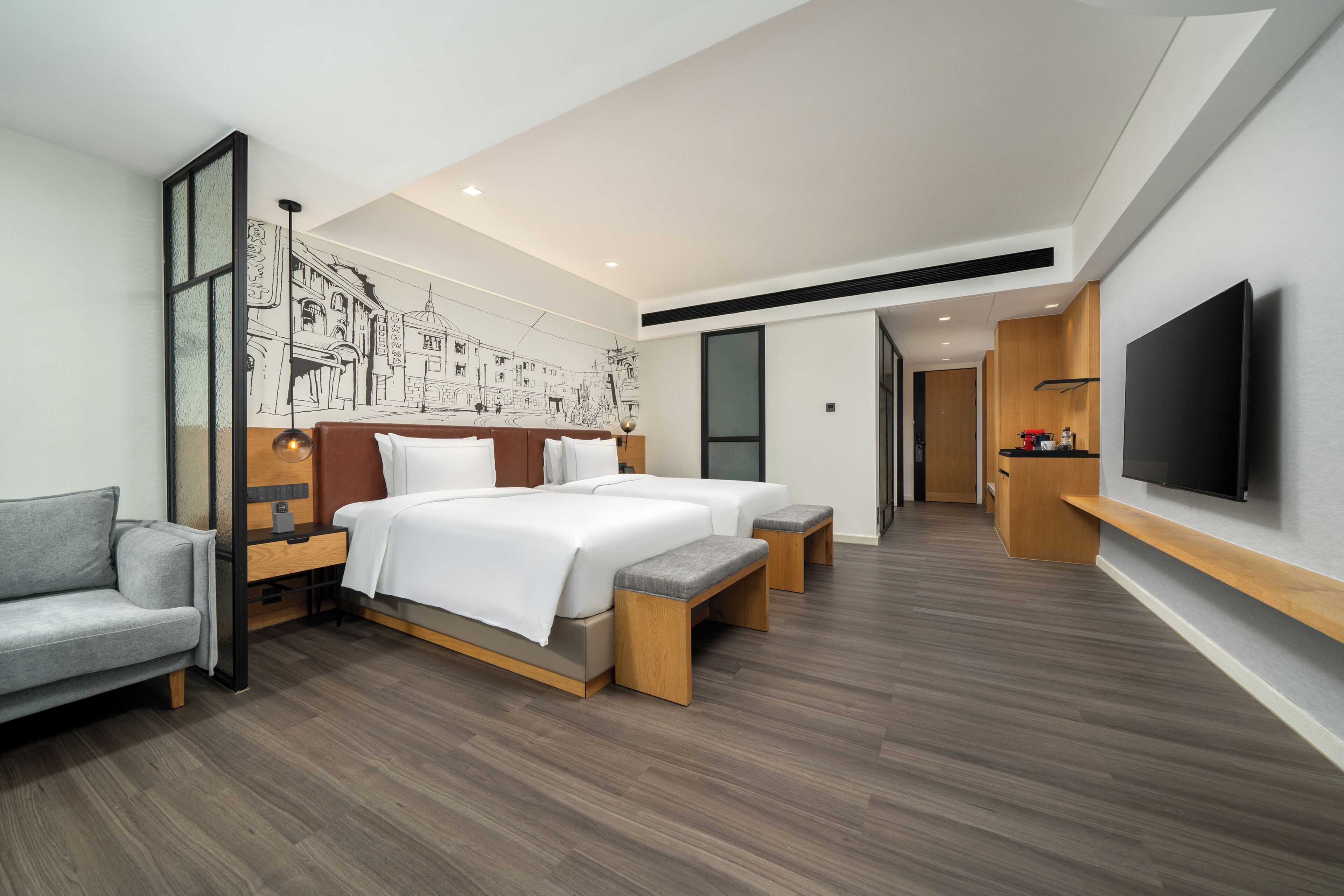 A modern hotel room with a large bed, a sofa, a TV, and a mural on the wall.