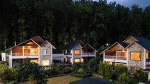 A row of modern, multi-story houses with balconies, surrounded by dense forest. - Megha Resort & Villas, Dehradun-Where Nature Pampers You (Vikasnagar)