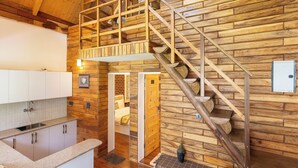 A rustic cabin interior with a wooden staircase, a kitchen area, and a loft bedroom. - Megha Resort & Villas, Dehradun-Where Nature Pampers You (Vikasnagar)