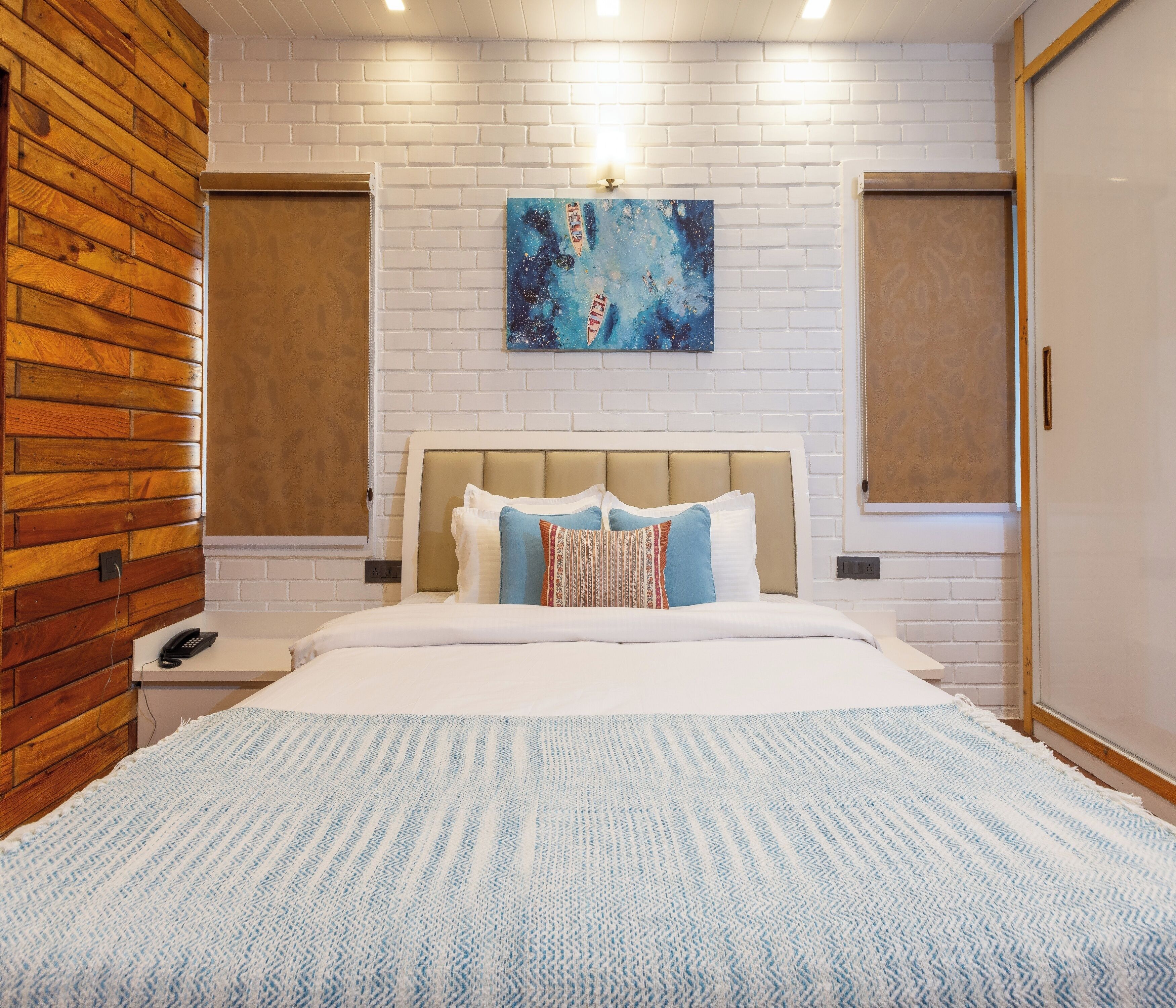 A hotel room with a bed, a nightstand, a telephone, a painting on the wall, and a wooden wall panel.