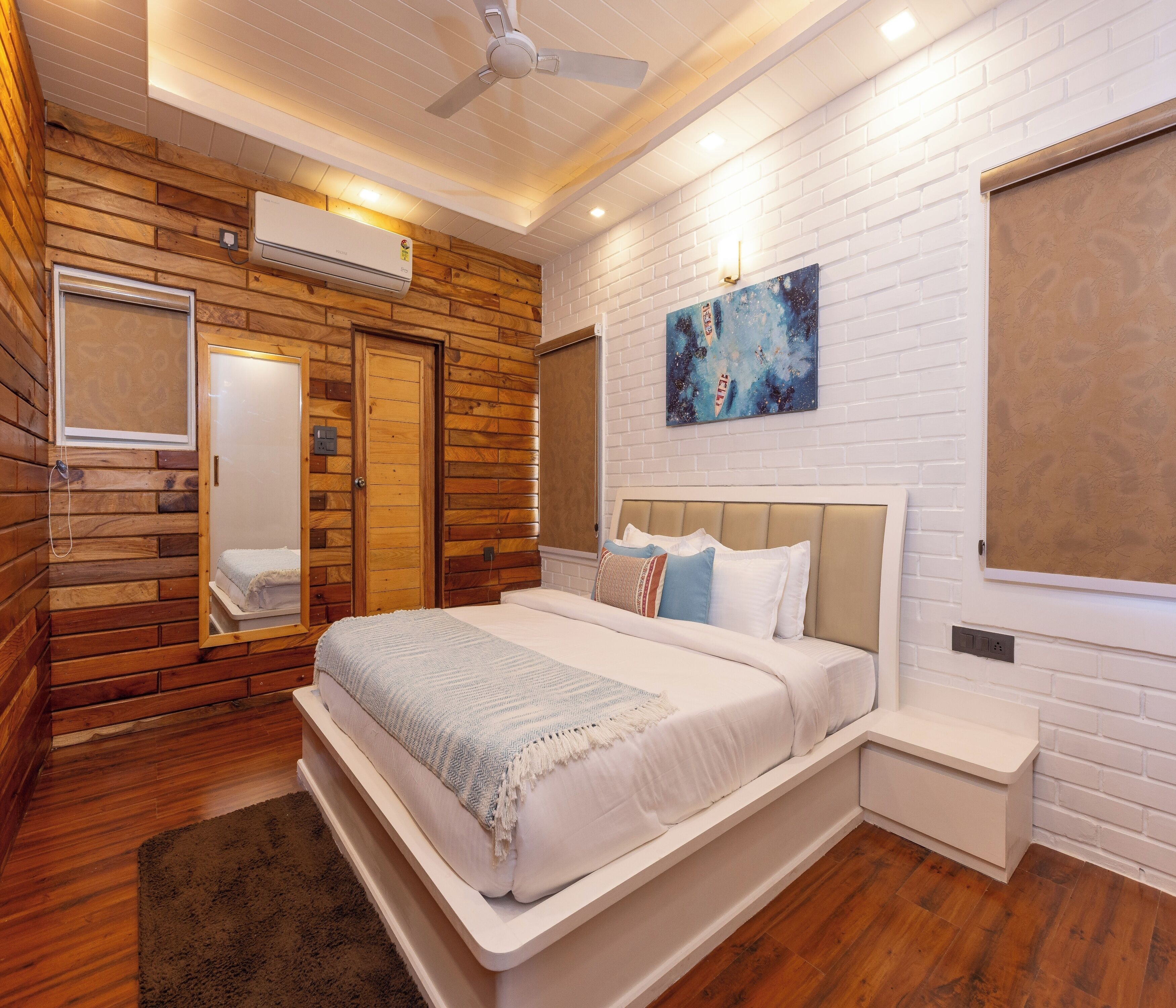 Un dormitorio con pared de madera, cama con ropa de cama blanca, mesita de noche y ventilador de techo.