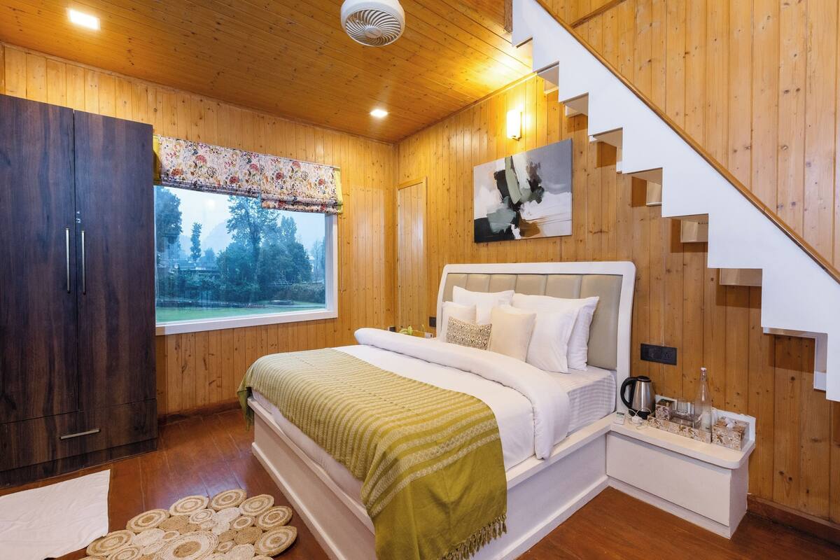 A wooden interior with a bed, a staircase, and a window with a view of trees.