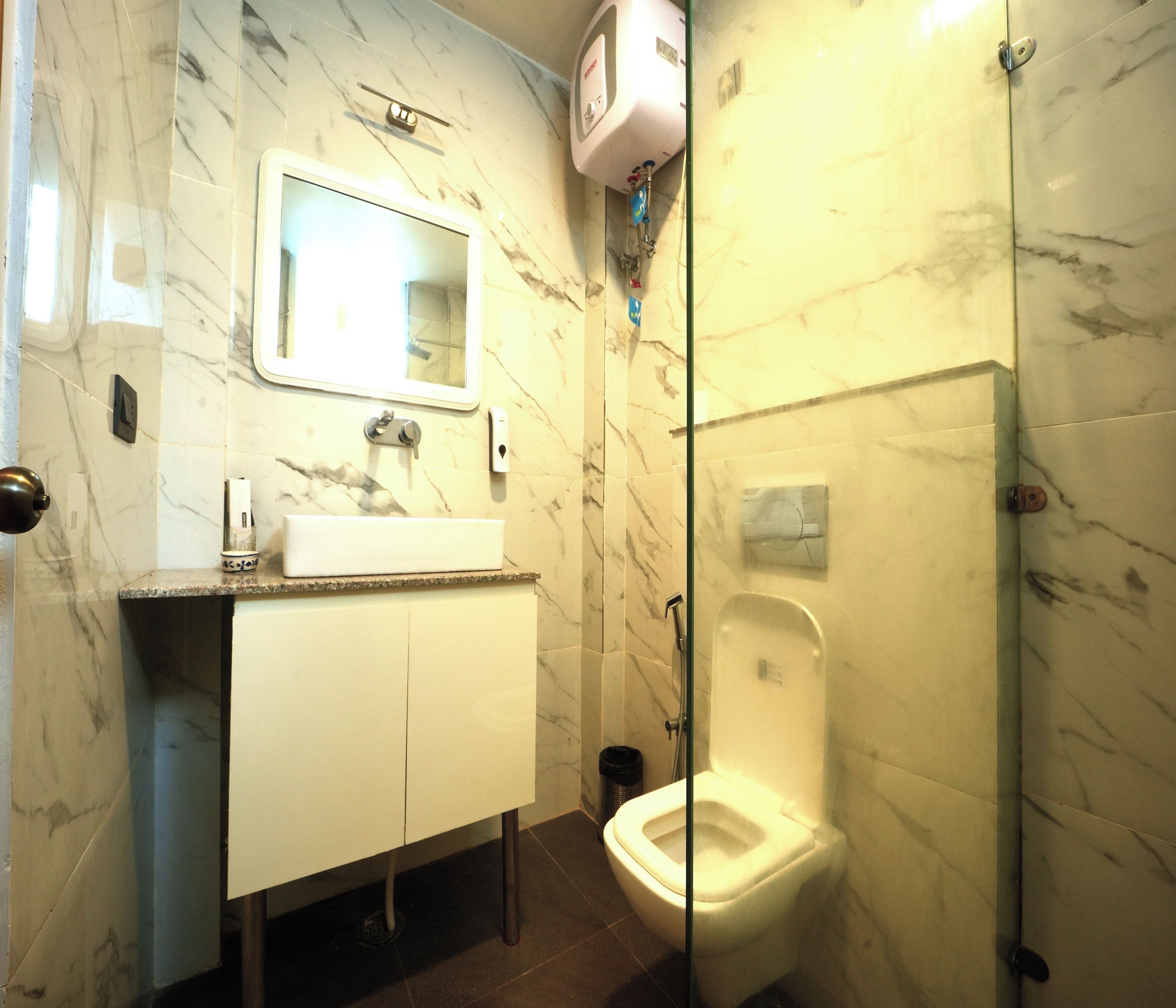 Ein Badezimmer mit Marmorwand, Waschbecken, Spiegel, Toilette und Duschbereich.