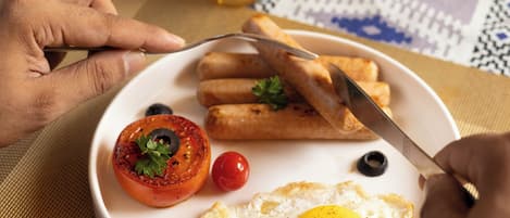 A breakfast plate with eggs, tomatoes, olives, and bread rolls.