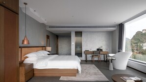 A modern bedroom with a large bed, a desk, a chair, and a view of a mountain. - YAOJIA WANGPU VILLA (Anshun)