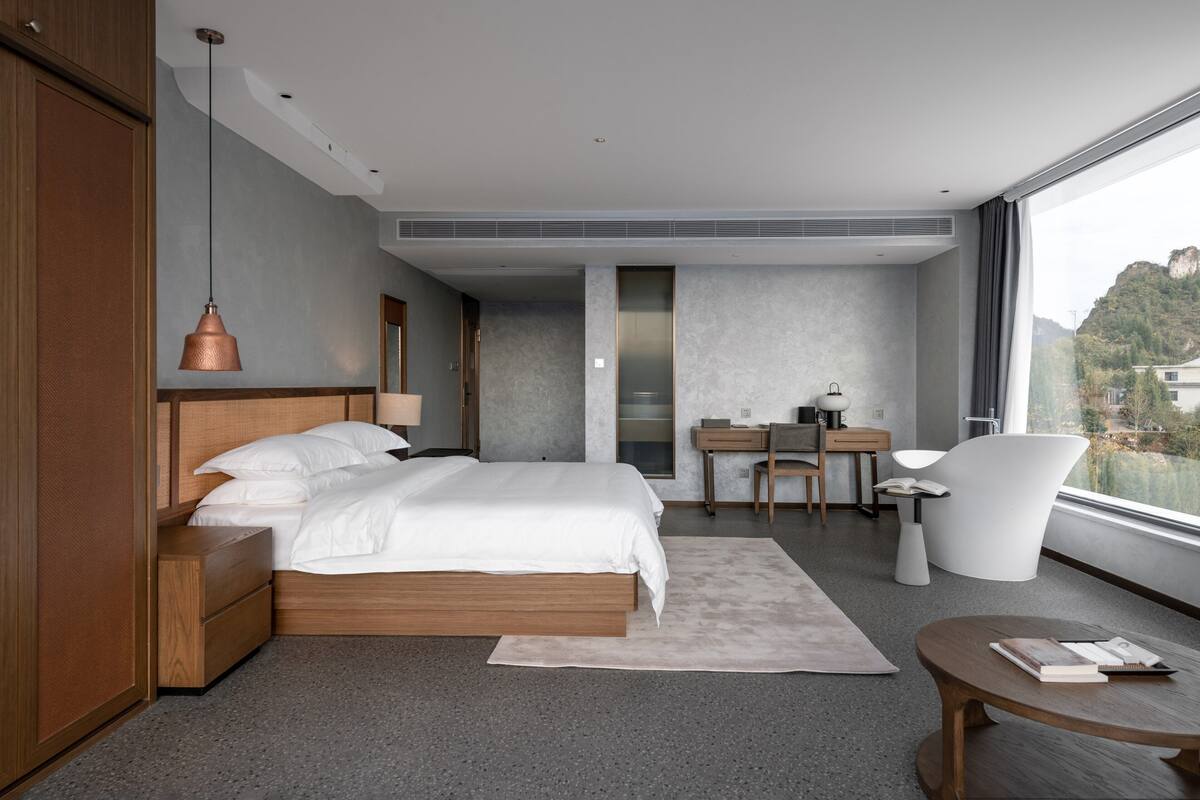 A modern bedroom with a large bed, a desk, a chair, and a view of a mountain.