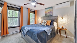 Ein Schlafzimmer mit Bett, Deckenventilator, Nachttisch und einem Fenster mit Vorhängen.