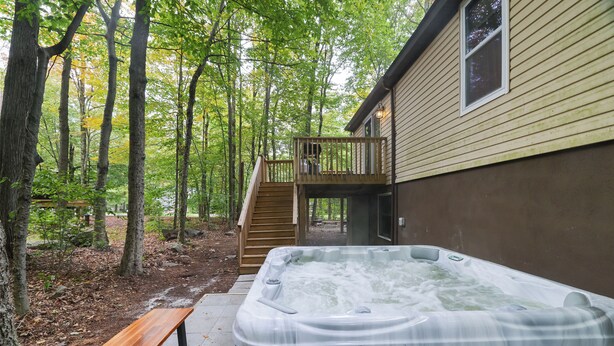Ein Whirlpool in einer bewaldeten Gegend mit einer Holzterrasse und einer Treppe, die zu einem Haus führt.