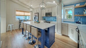 A modern kitchen with a central island, bar stools, and a window with a view. - Seaglass Landing | Private Pool, Cabana, & Near Port Aransas Beaches (Port Aransas)