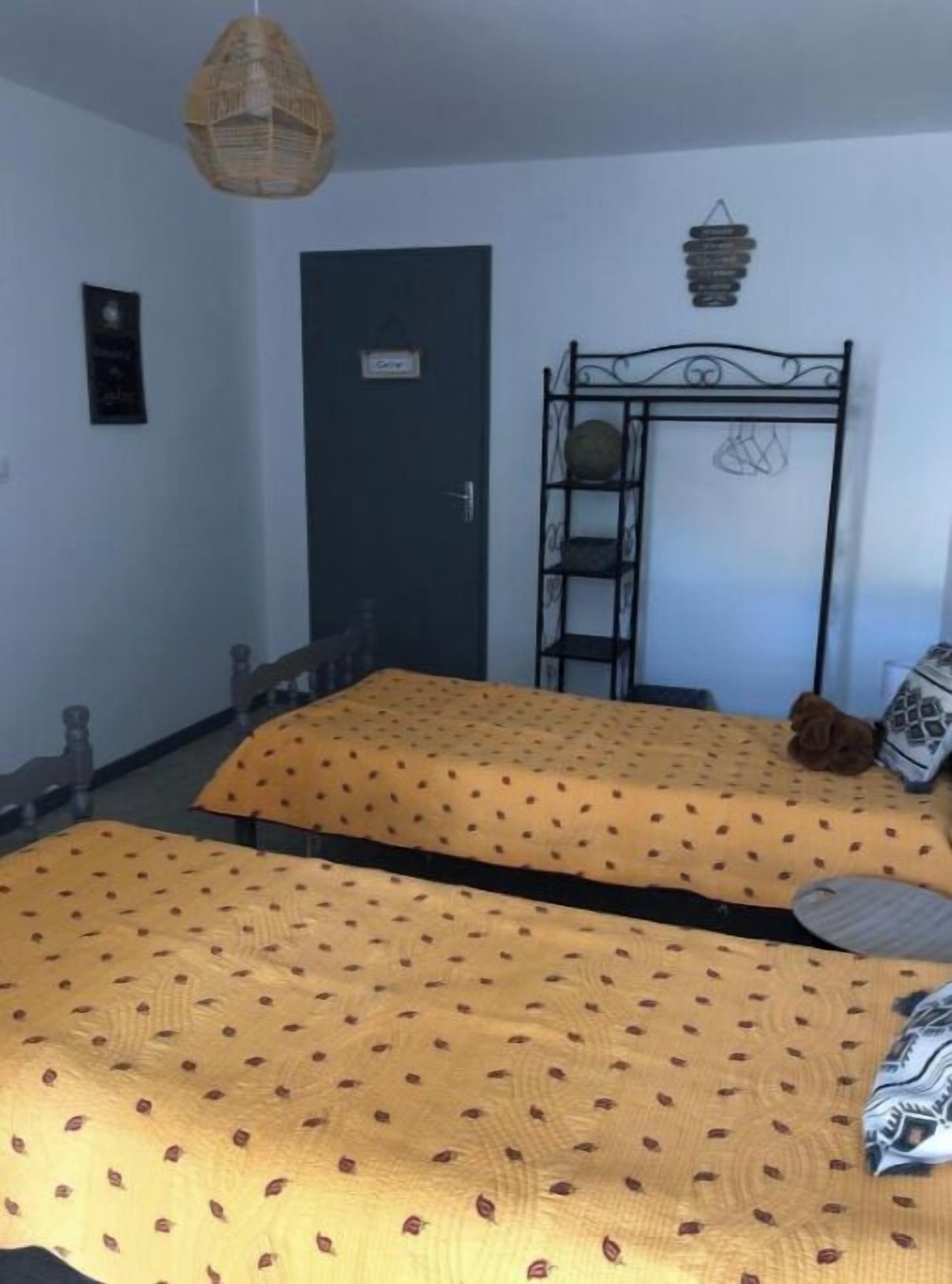 Ein Zimmer mit zwei Betten, einer Tür, einer Hängelampe und einem Regal mit Dekoration.