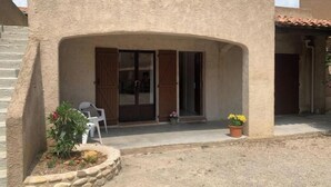 A building with a stone facade, a covered entrance with a bench, and a small garden area with plants. - Le Cigalou (Sainte-Croix-du-Verdon)