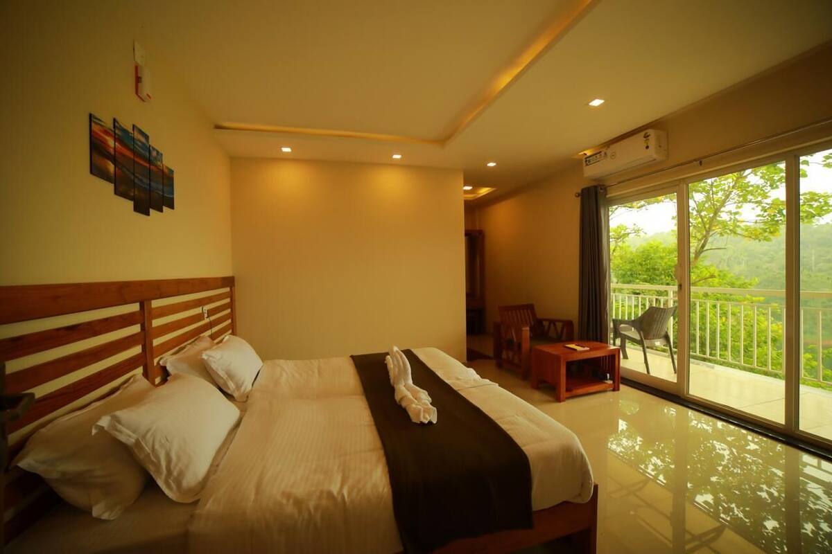A hotel room with a large bed, a balcony with a view, and a small seating area.