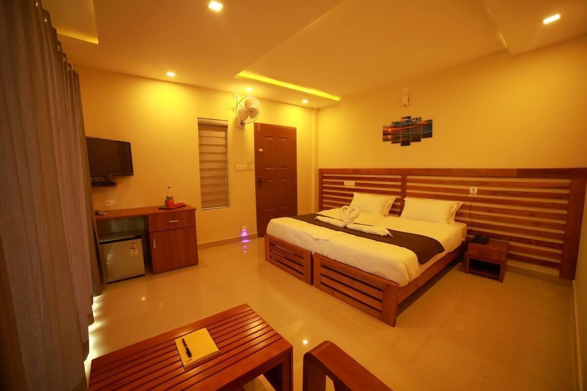 A hotel room with a bed, a desk, a chair, a TV, and a door.