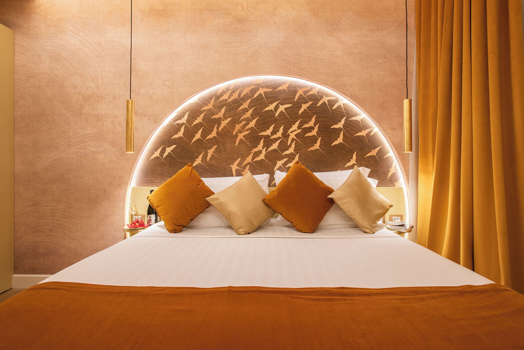 Una habitación de hotel con techo de diseño curvo, cama con ropa blanca y cabecera con estampado de pájaros.