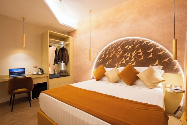 A hotel room with a large bed, a desk with a laptop, a wardrobe, and a circular headboard with a bird design.