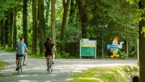 Ein gepflasterter Weg mit Radfahrern, umgeben von Bäumen und Grünflächen, mit einem Schild für 'Pruwinkel' und einem Parkschild.