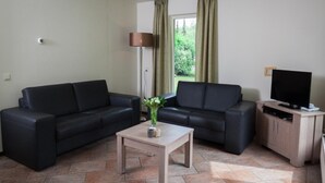 Ein Wohnzimmer mit zwei schwarzen Sofas, einem kleinen Holztisch mit einer Vase, einer Lampe und einem Fernseher auf einer Holzkommode.