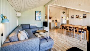 Ein modernes Wohnzimmer mit einer Eckcouch, einem Essbereich mit Holzsesseln und einer Küche im Hintergrund.