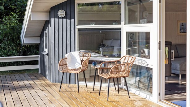 Ein gemütlicher Außenbereich mit Korbmöbeln und einem Tisch, mit Blick auf ein Schlafzimmer mit Bett und Fenster.