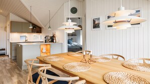 Eine moderne Küche mit einer zentralen Kochinsel, Pendelleuchten und einem Essbereich mit einem Holztisch und gewobenen Tischsets.
