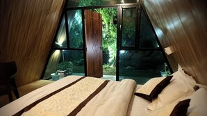A cozy bedroom with a large bed, a wooden door, and a view of greenery outside. - Camp Mountain Valley (Dhanaulti)