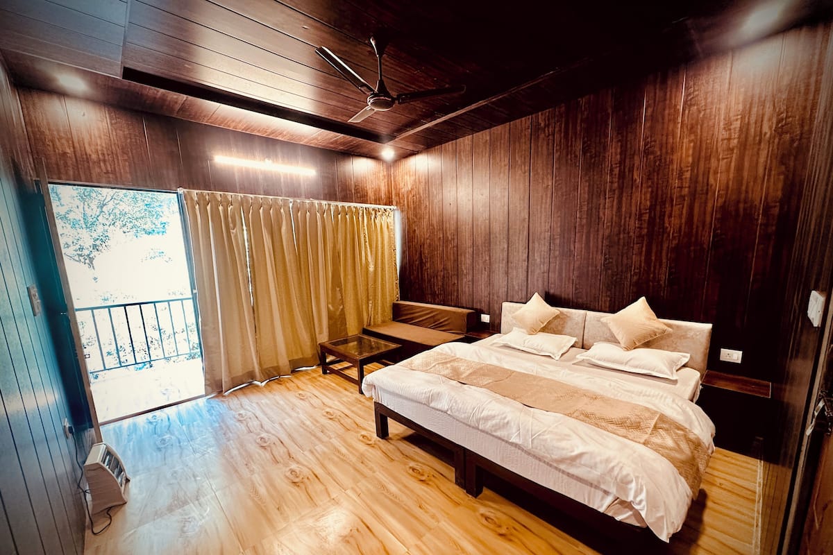 Un dormitorio con suelo de madera, una cama con muchos cojines, una mesita y un ventilador de techo.