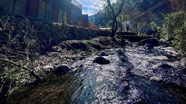 A riverside view with a building featuring balconies and a stone wall. - Camp Mountain Valley (Dhanaulti)