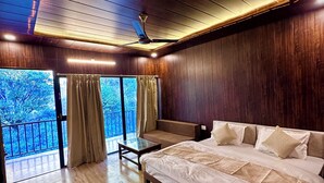 A spacious bedroom with a large bed, a nightstand, a wooden floor, and a balcony with curtains. - Camp Mountain Valley (Dhanaulti)