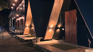 A modern building with a unique triangular design, featuring large wooden panels and a staircase leading to an upper level. - Camp Mountain Valley (Dhanaulti)