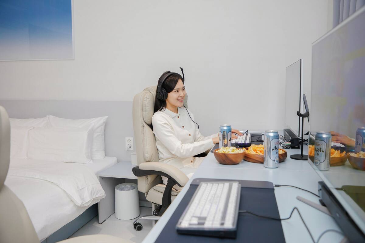A hotel room with a bed, a desk with a computer, a chair, and a bowl of popcorn and cans of beer.