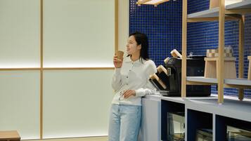 A person standing in a room with a blue tiled wall, holding a cup. There is a sign above that reads "SELF LOUNGE".
