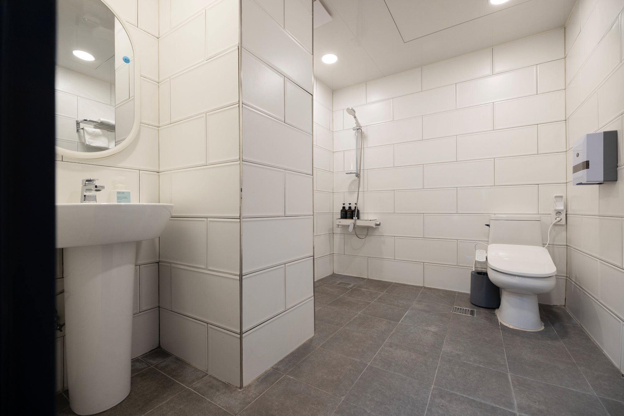 A modern bathroom with white tiles, a sink, a toilet, and a shower.