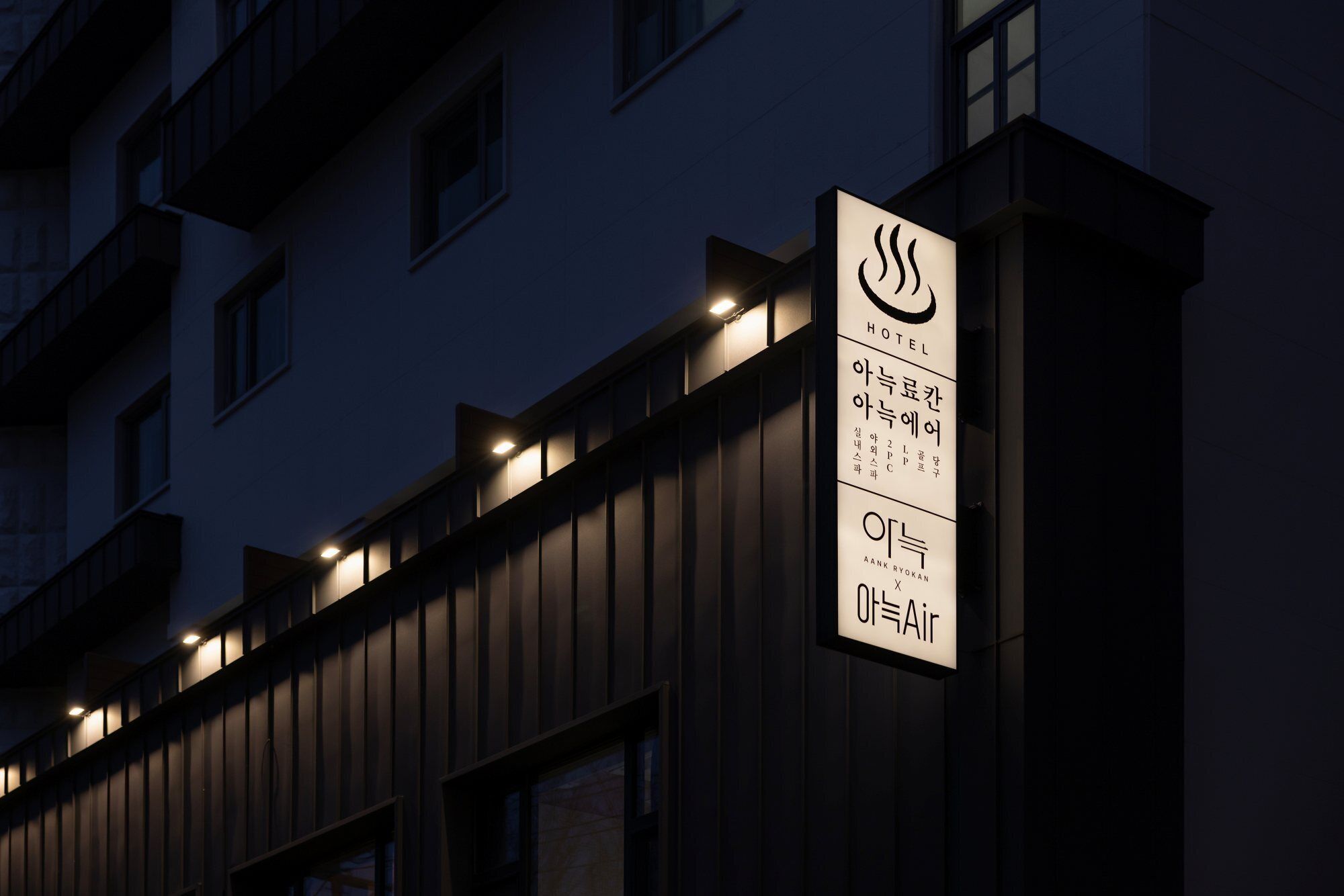 A hotel sign with Korean text and a logo, indicating a modern building facade with multiple windows and lights.