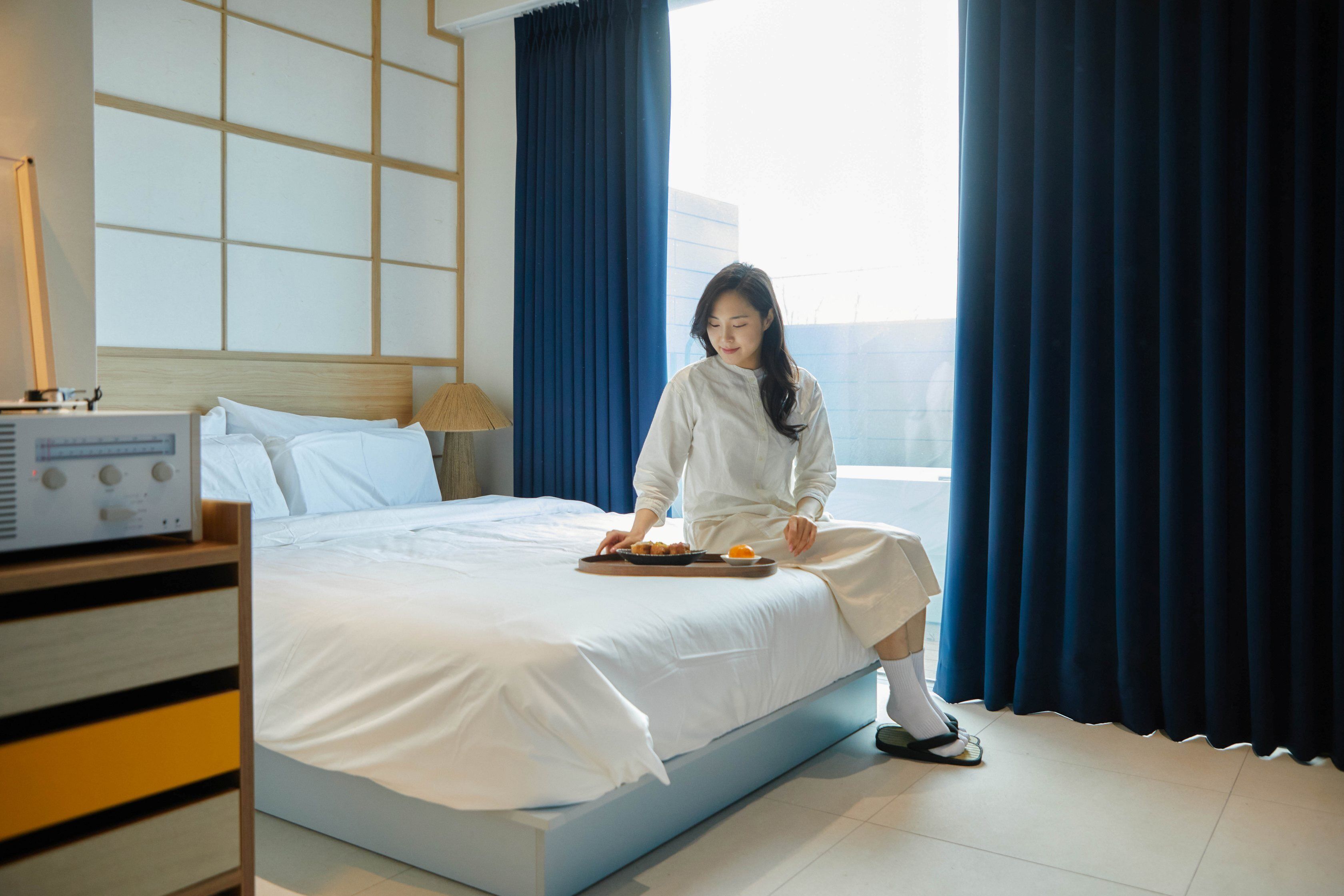A hotel room with a bed, a radio, and a window with curtains.