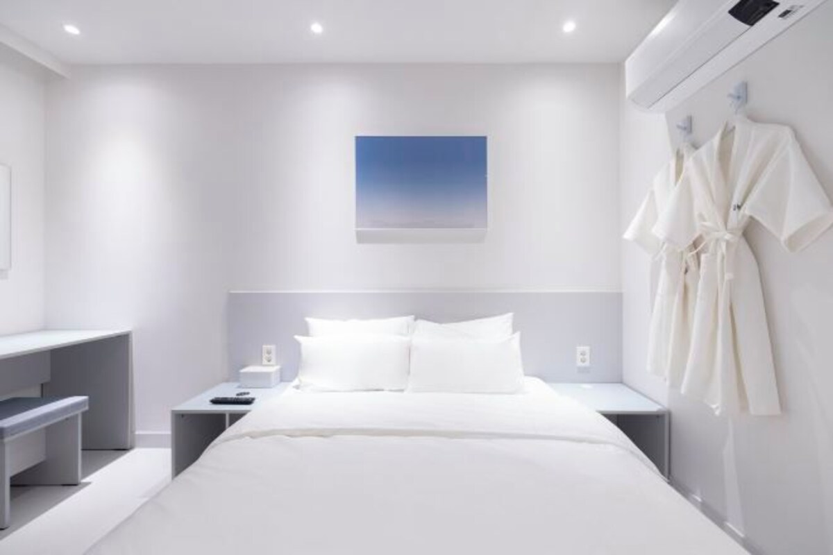 A modern hotel room with a large bed, bedside tables, a desk, and a robe hanging on the wall.