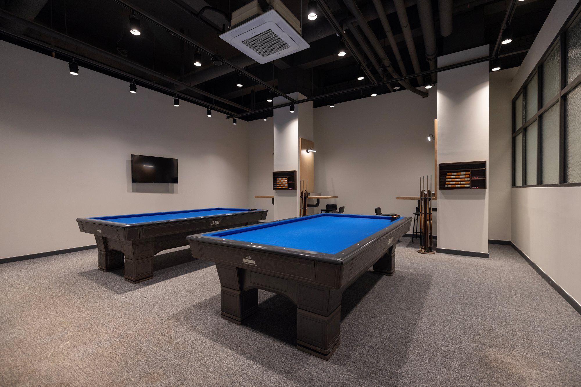 A pool table area with two pool tables, a television, and a billiards rack.