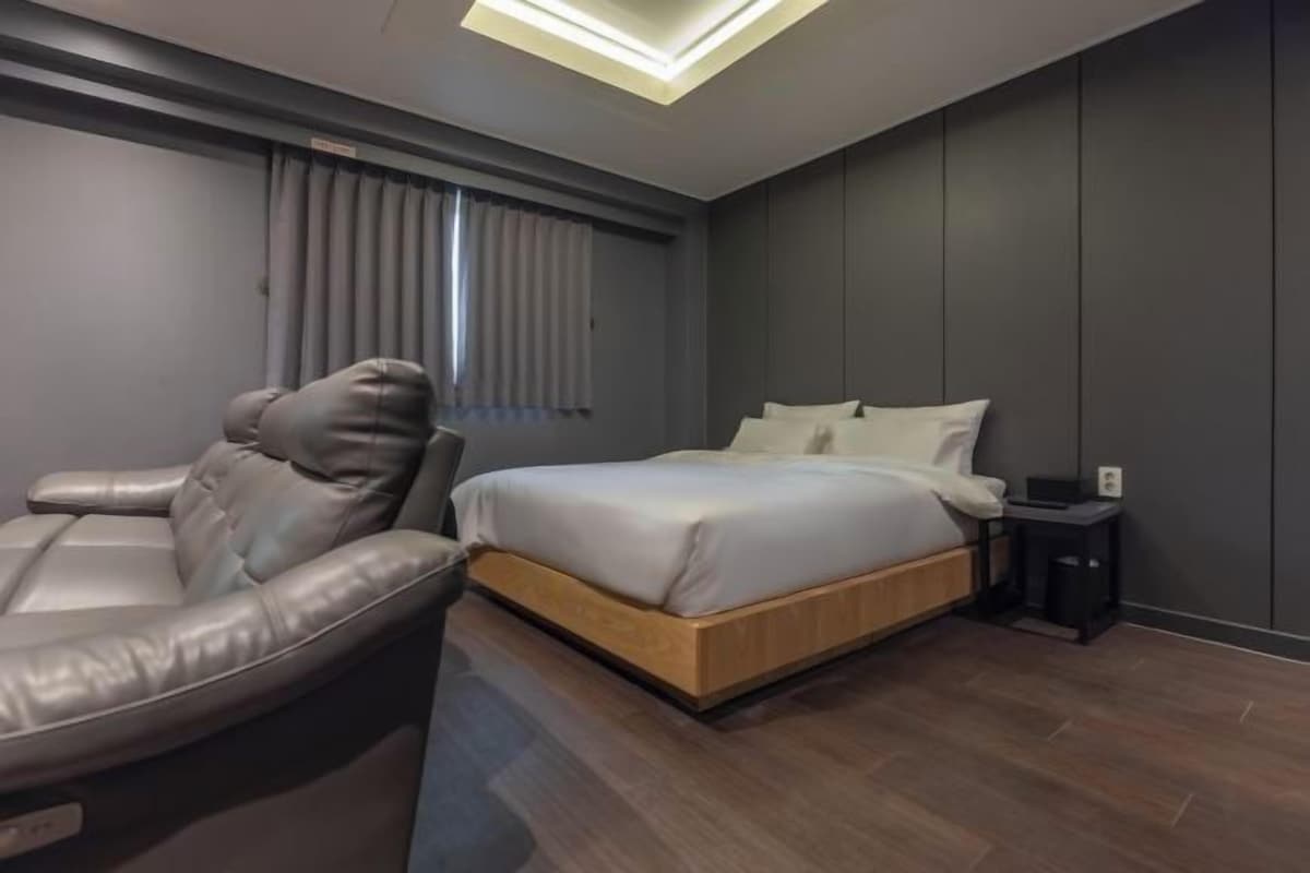 A modern bedroom with a bed, a massage chair, and a small bedside table.