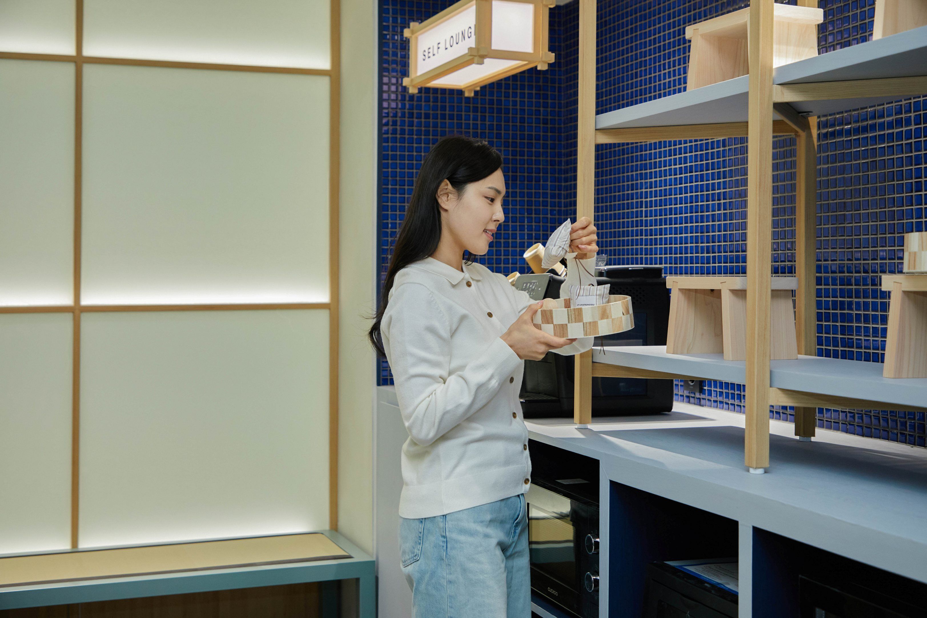 A person holding a box in a room with blue tiled walls and wooden shelves.
