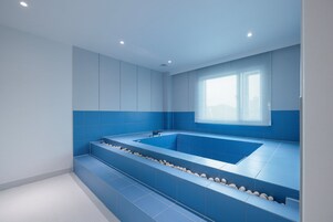 Un baño moderno con una bañera grande, azulejos azules y una ventana con persianas.