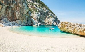 Een strand met helder turquoise water, wit zand en rotsachtige kliffen.